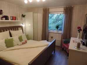 Een keurig opgemaakt slaapkamer met een bed, nachtkastje en een raam met gordijnen.