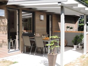 Een overdekt terras met een tafel, stoelen, een potplant en uitzicht op het interieur van het huis.