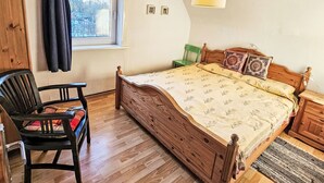 Un dormitorio con una cama de madera, una silla, una ventana con cortinas, una lámpara y una mesita.