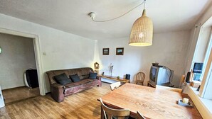 Una sala de estar con un sofá de cuero marrón, una mesa de comedor de madera y sillas, un televisor y una lámpara colgante.