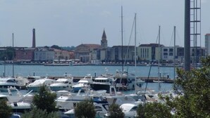 Uma marina com vários barcos atracados, uma igreja destacada com uma torre alta e edifícios industriais ao fundo.