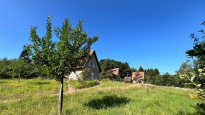 Ein Haus aus Stein mit geneigtem Dach, umgeben von einem grasbewachsen Feld und Bäumen.