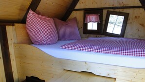 Quarto de cabana de madeira aconchegante, com uma cama, roupa de cama xadrez e uma pequena janela com cortina xadrez.