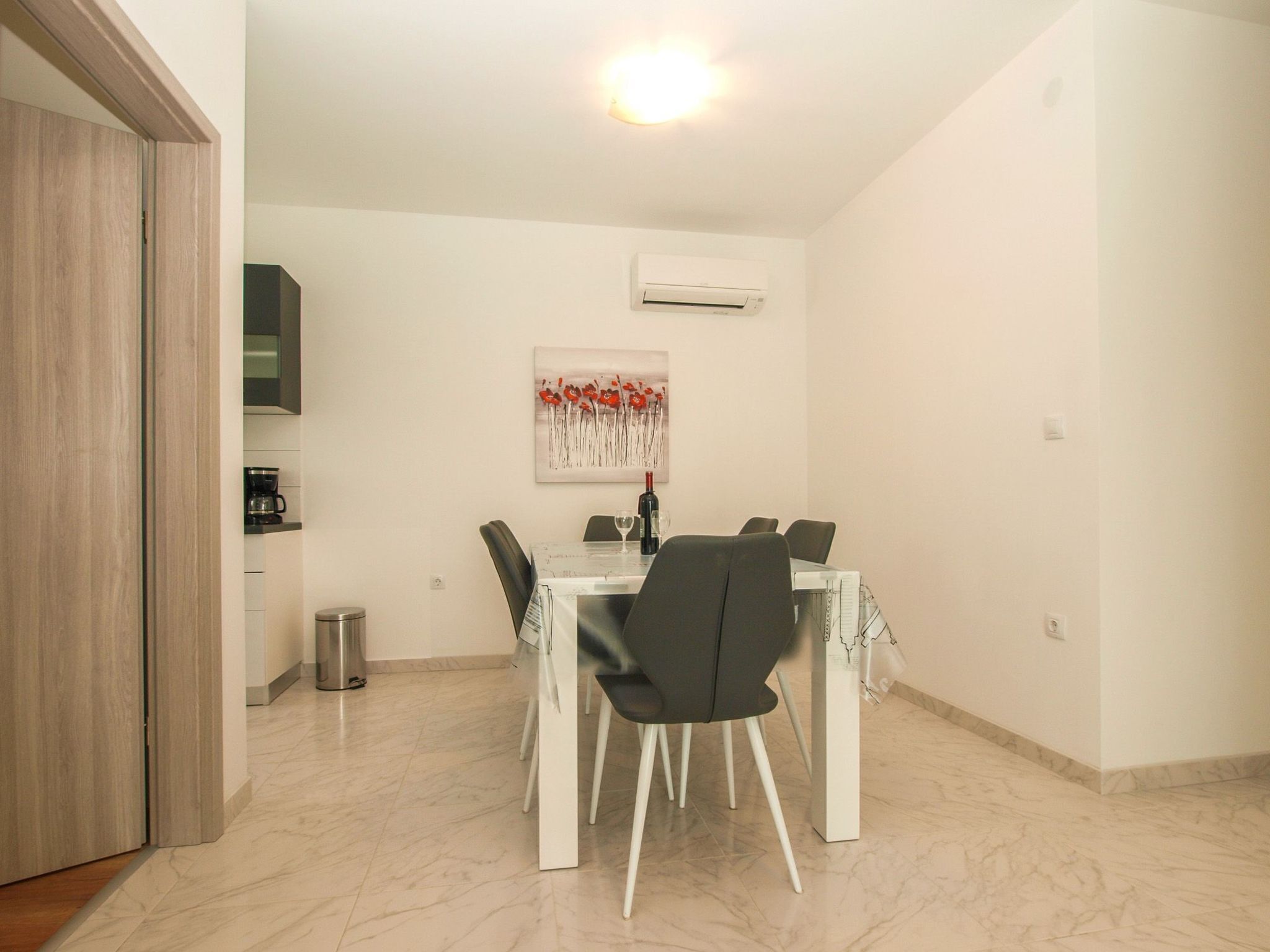 A dining area with a table and chairs, an air conditioning unit on the wall, and a trash can.