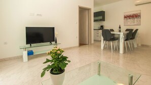 Una sala moderna con televisor de pantalla plana, una mesa de comedor con sillas, una zona de cocina y una planta en maceta.