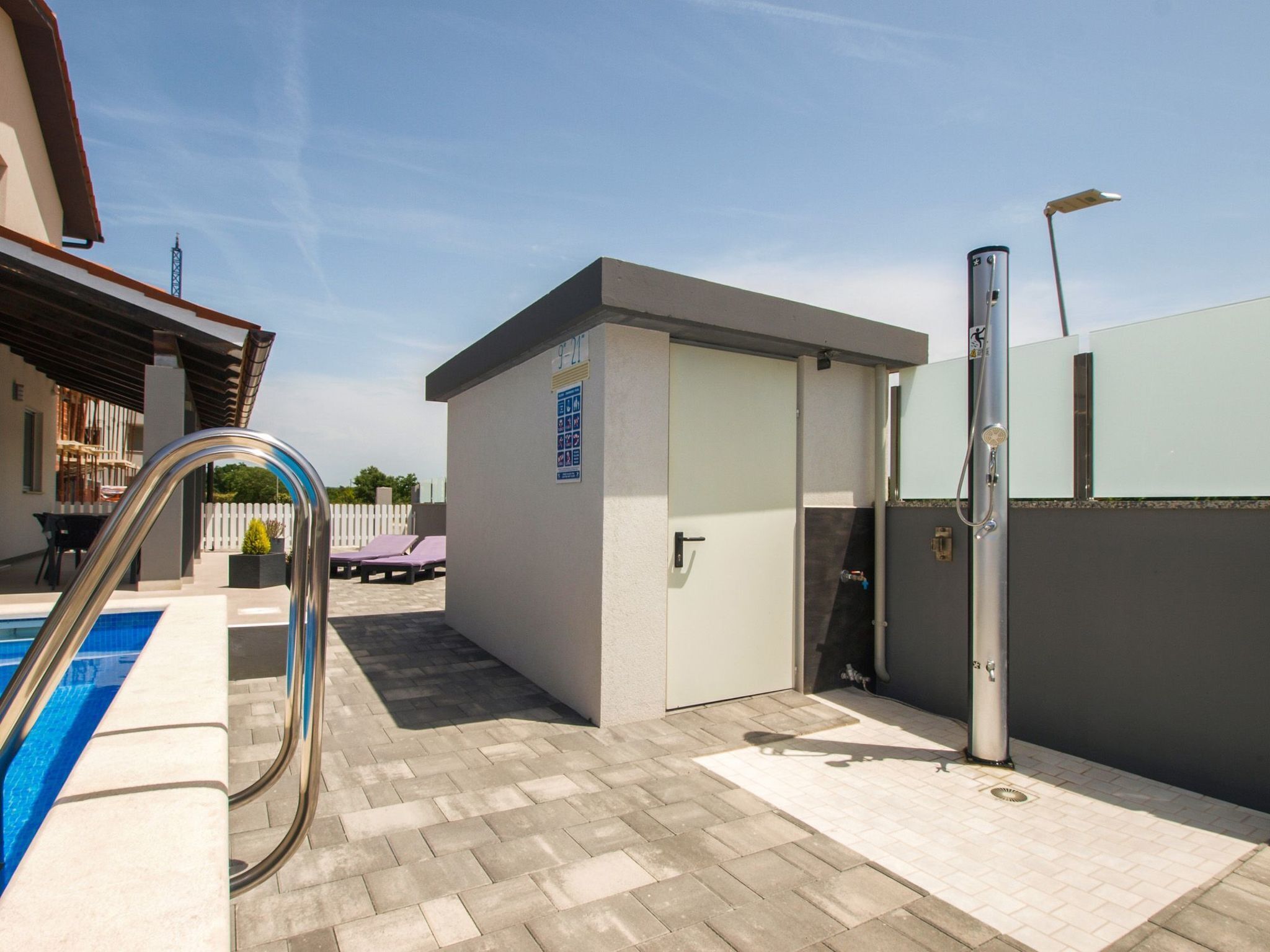Área de piscina com escada de metal, porta e chuveiro.