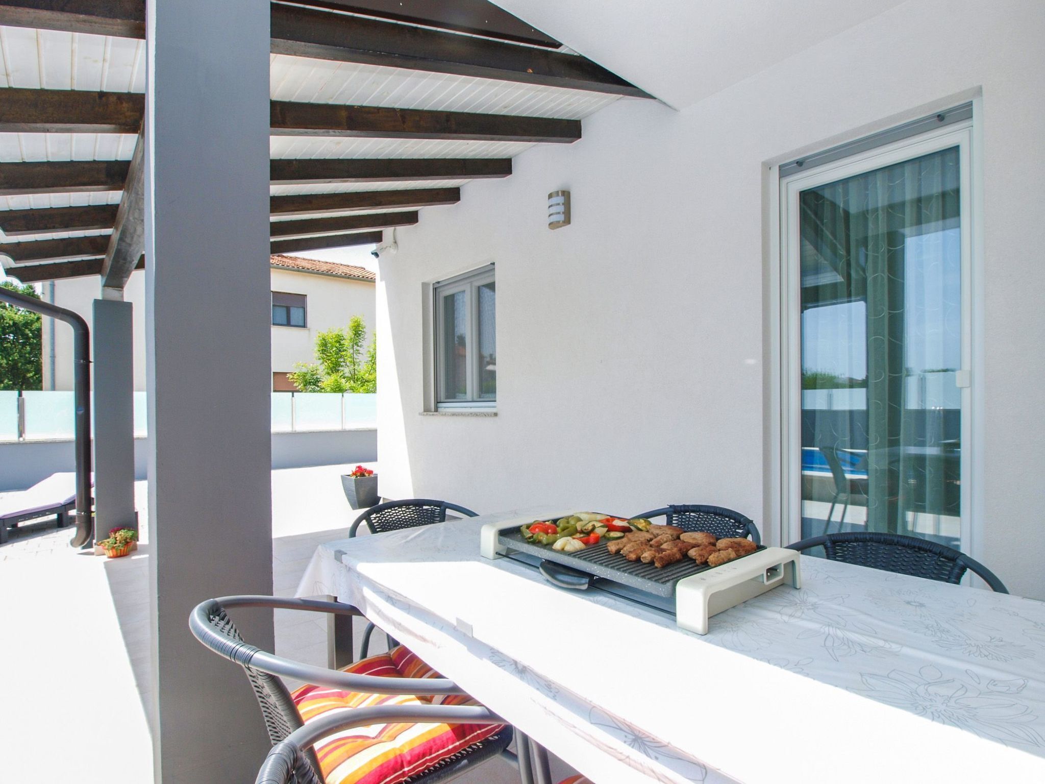 An outdoor patio with a table set for dining, a grill with food, and a view of the surrounding buildings.