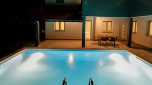 Piscina con zona de patio, que incluye una mesa y sillas, y una sección cubierta con ventanas.
