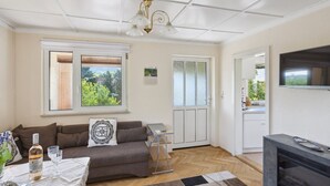 Una sala de estar con sofá, una mesa de centro, chimenea, televisor y ventana con vista a follaje.