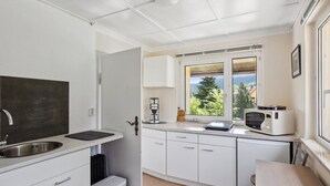 Cocina compacta con armarios blancos, un lavamanos, una cafetera, un microondas y una ventana con vistas a árboles y montañas.