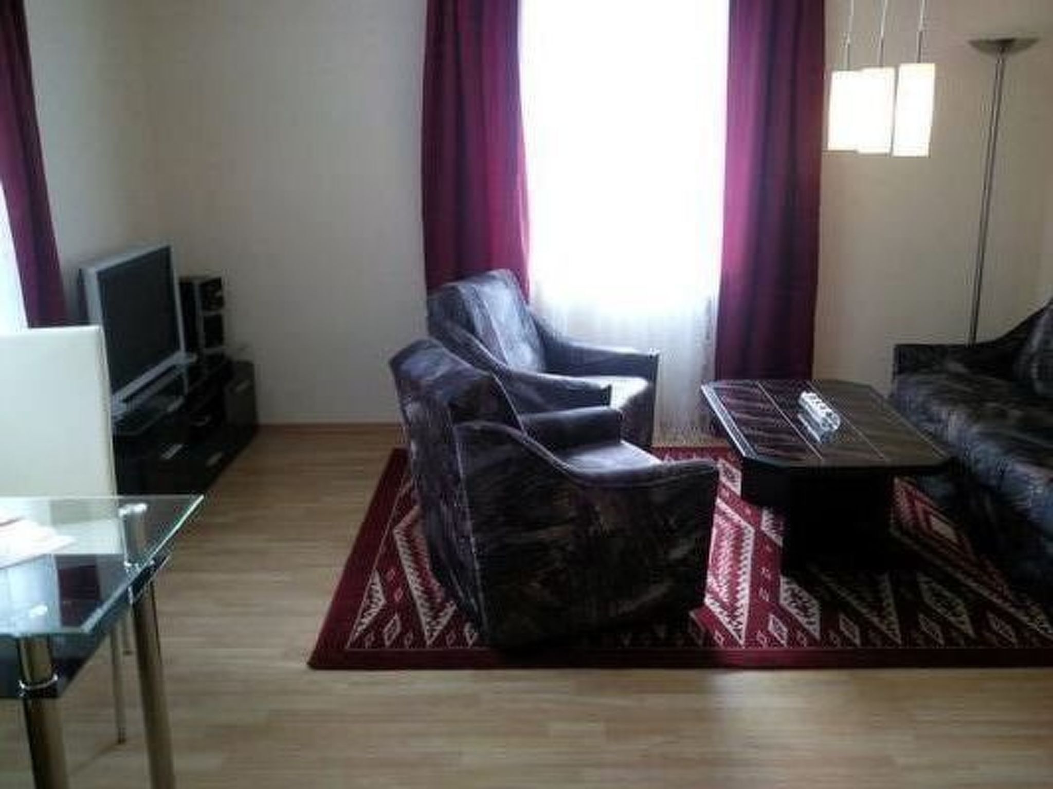Uma sala de estar com sofá, duas poltronas, uma mesa de centro, televisão e uma mesa de vidro.