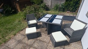 Eine Terrassenfläche im Freien mit Tisch und vier Stühlen, umgeben von einem Kiesboden und Grünpflanzen.