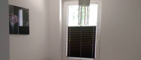 A bedroom with a bed, a window with blinds, a hanging light fixture, and a framed picture on the wall.