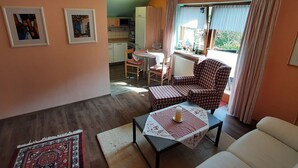 A cozy living room with a checkered armchair, a sofa, and a dining table with a red and white tablecloth. There is a kitchen in the background with a microwave and a kettle. - Seitz 1 in Bayerisch Eisenstein by Interhome (Bayerisch Eisenstein)