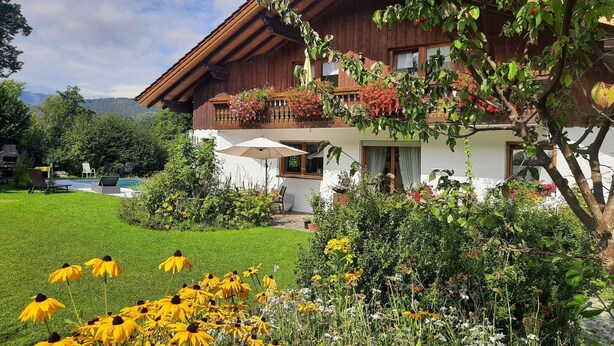 A two-story chalet with a wooden exterior, a balcony with flowers, a pool, and a well-maintained garden with yellow flowers. - Seitz 1 in Bayerisch Eisenstein by Interhome (Bayerisch Eisenstein)