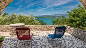 A patio with a stone arch, two chairs, and a table overlooking a lake. - Biserka by Interhome (Krk/Čižići)