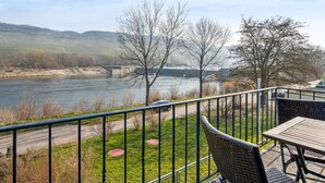 A riverside view from a balcony with a table and chairs, a railing, and a path leading to a bridge. - mit Balkon und schönem Moselblick by Interhome (Klüsserath)