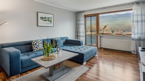 A modern living room with a blue sofa, a coffee table, and a view of a countryside landscape through a large window. - mit Balkon und schönem Moselblick by Interhome (Klüsserath)