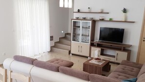 A modern living room with a sofa, coffee table, and TV stand. There is a staircase with glass doors leading to a balcony. - in Banjole mit Privatem Pool by Interhome (Pula/Banjole)