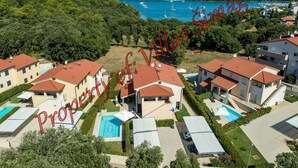 A residential area with multiple houses, each featuring a red-tiled roof and a swimming pool. The houses are surrounded by lush greenery, and there is a view of a bay with boats in the distance. - in Banjole mit Privatem Pool by Interhome (Pula/Banjole)