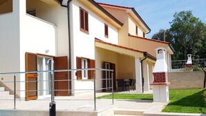 Ein zweistöckiges Haus mit einer überdachten Terrasse, einem Swimmingpool und einem Ziegelkamin.