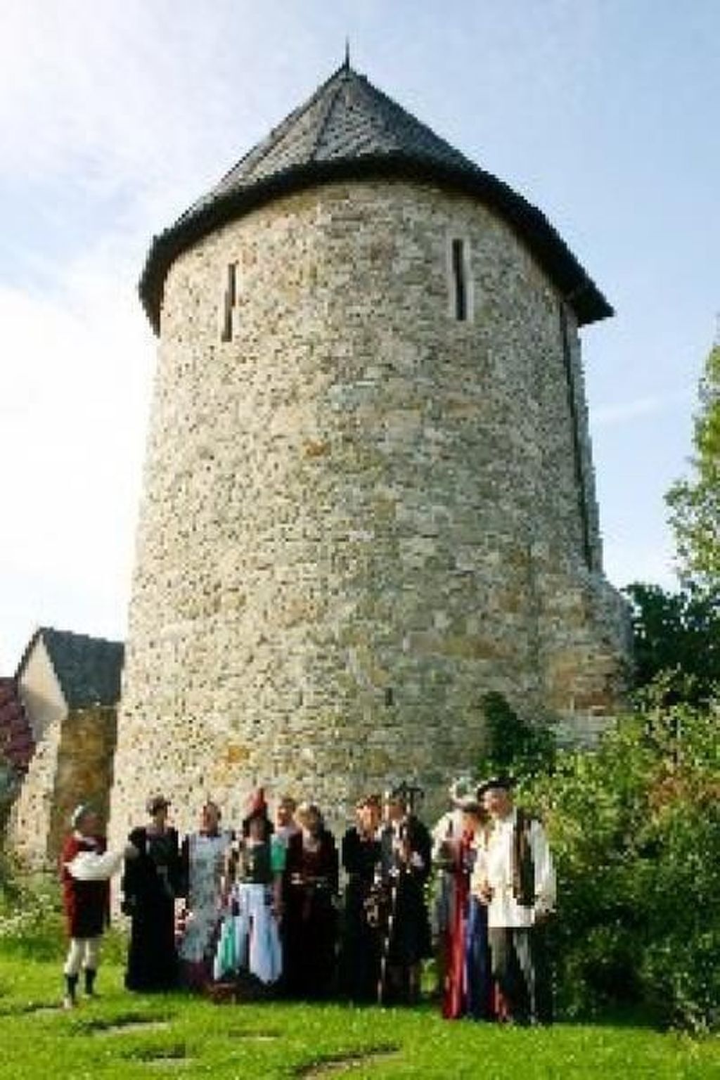 A stone tower with a conical roof, surrounded by a group of people in historical costumes.