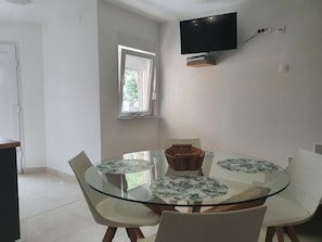 A dining area with a glass table and four chairs, a wicker basket, and a flat-screen TV mounted on the wall. - Schönes Apartment in Banjole mit Terrasse by Interhome (Pula/Banjole)