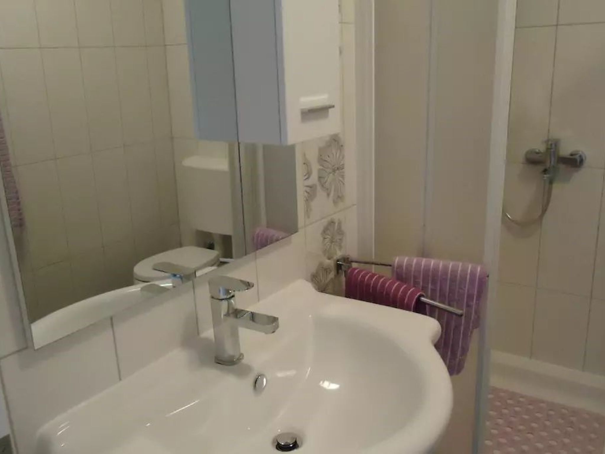 A bathroom with a white sink, a mirror, a toilet, and a shower area.