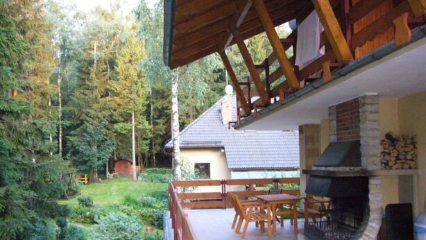 A covered patio with a stone fireplace, wooden furniture, and a view of a house and forest. - "Villa Petra" mit eigener Terrasse by Interhome (Karpacz)