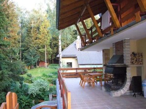 A covered patio with a stone fireplace, wooden furniture, and a view of a house and forest. - "Villa Petra" mit eigener Terrasse by Interhome (Karpacz)