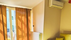 Una habitación de hotel con cama, sofá, una mesa con copas de vino y una botella, y una ventana con cortinas.