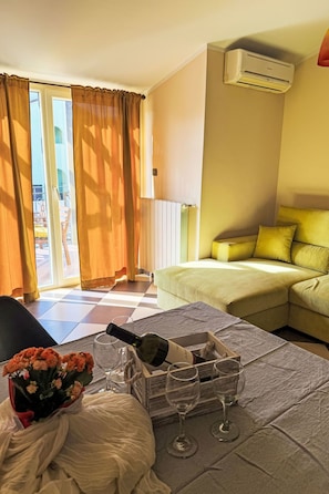 Ein Hotelzimmer mit Bett, einer Couch, einem Tisch mit Weingläsern und einer Flasche sowie einem Fenster mit Vorhängen.