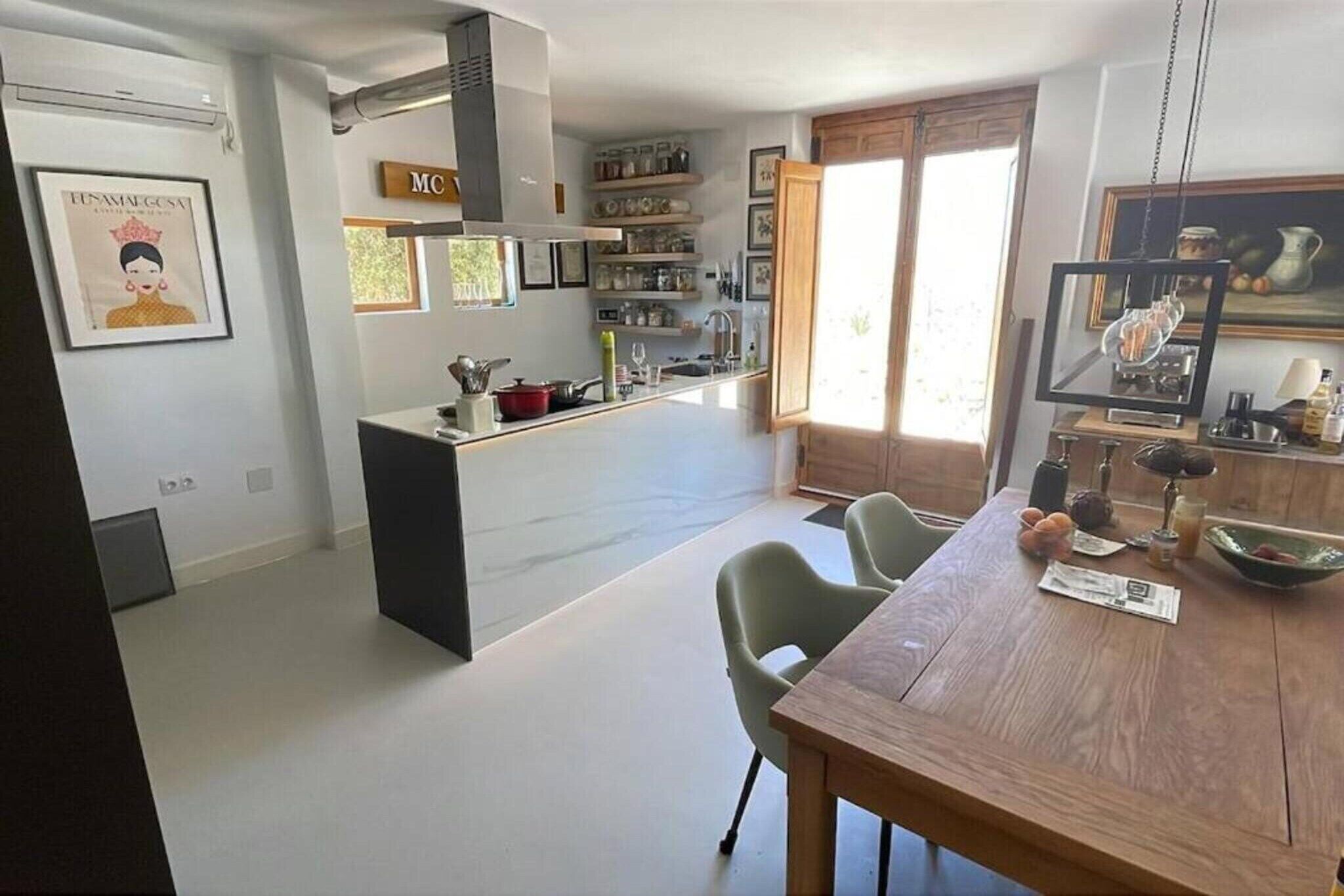 A modern kitchen with a central island, a dining area with a wooden table and chairs, and a kitchen counter with various items.