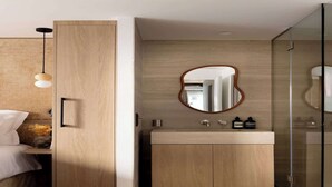 Un baño moderno con un mueble tocador de madera, un espejo redondo y una cabina de ducha de vidrio.