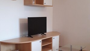 Una sala de estar con un televisor sobre un mueble de madera, una mesa de centro de vidrio y un sofá color crema.