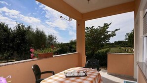 Un patio cubierto con una mesa para dos, rodeado de sillas, con vistas a un jardín con árboles y flores.