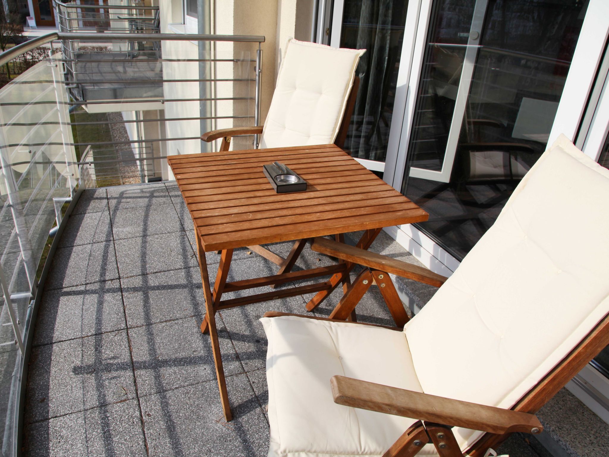 A wooden table and two chairs on a balcony with a glass railing.