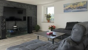 Una sala de estar moderna con televisor de pantalla plana, una mesa de centro de vidrio, un sofá gris y un cuadro en la pared.