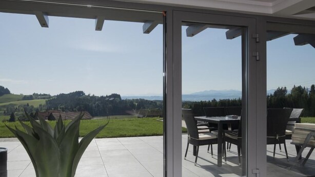 Un patio moderno al aire libre con una puerta de vidrio que da a una vista panorámica de colinas y montañas ondulantes.