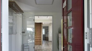 Un pasillo moderno con una escalera de madera, una puerta de cristal y una puerta roja.