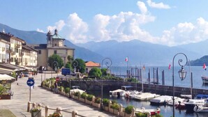 A waterfront marina with boats docked, a church with a bell tower, and mountains in the background. - Haus Antonini by Interhome (Brissago)