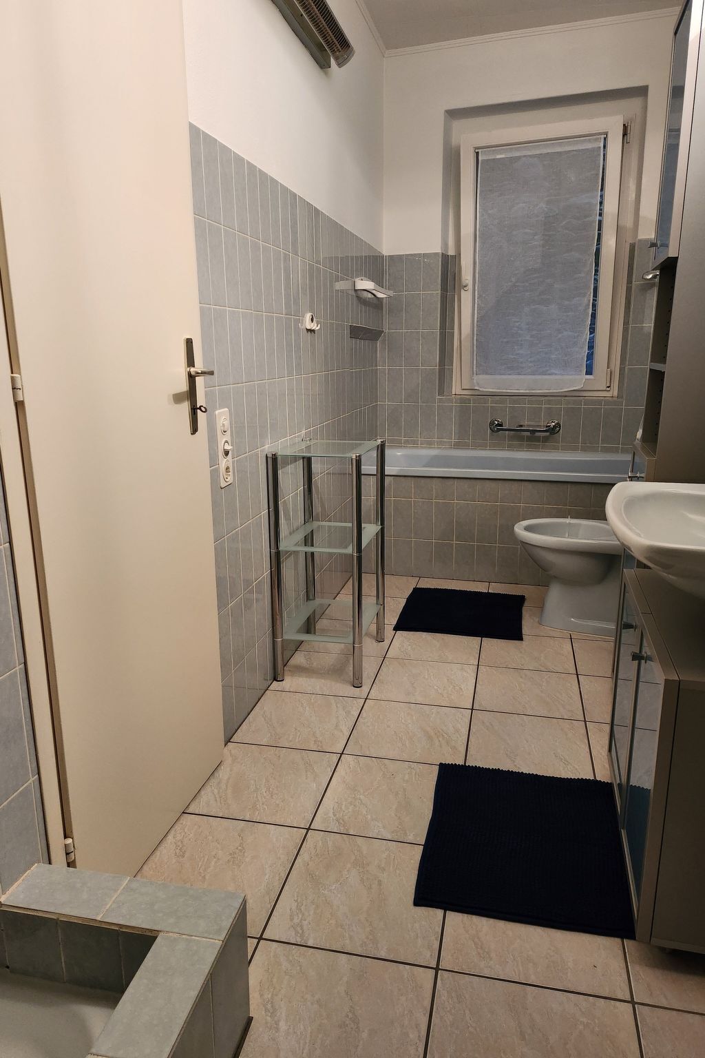 Ein Badezimmer mit Duschkabine aus Glas, einem weißen Waschbecken und einem Fenster über der Badewanne.