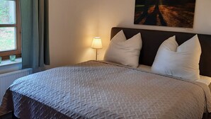 A neatly made bed with a quilted cover, a bedside lamp, and a painting of a forest scene on the wall. - Alte Kate by Interhome (Thomasburg)