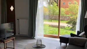 A living room with a television, a round table with a candle, a sofa, and a view of a garden and a brick building. - Alte Kate by Interhome (Thomasburg)