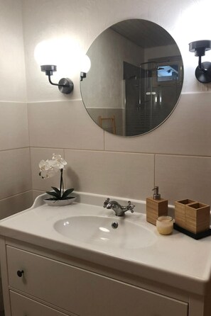 Ein Badezimmer mit rundem Spiegel, Waschbecken, kleiner Pflanze und Holzschatulle.