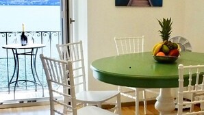A dining area with a green table, white chairs, and a fruit bowl. A painting of a mountain landscape is on the wall. - See-Penthouse by Interhome (Brissago)