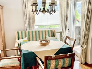 A dining area with a round table, striped upholstered chairs, a chandelier, and a view through a window. - Wohnung in Bergen und Panoramablick by Interhome (Bergen)