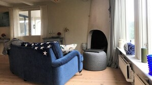 A cozy living room with a blue sofa, a small round ottoman, a fireplace, and a window with curtains. - "Torekov" mit Blick auf das Wasser by Interhome (Torekov)