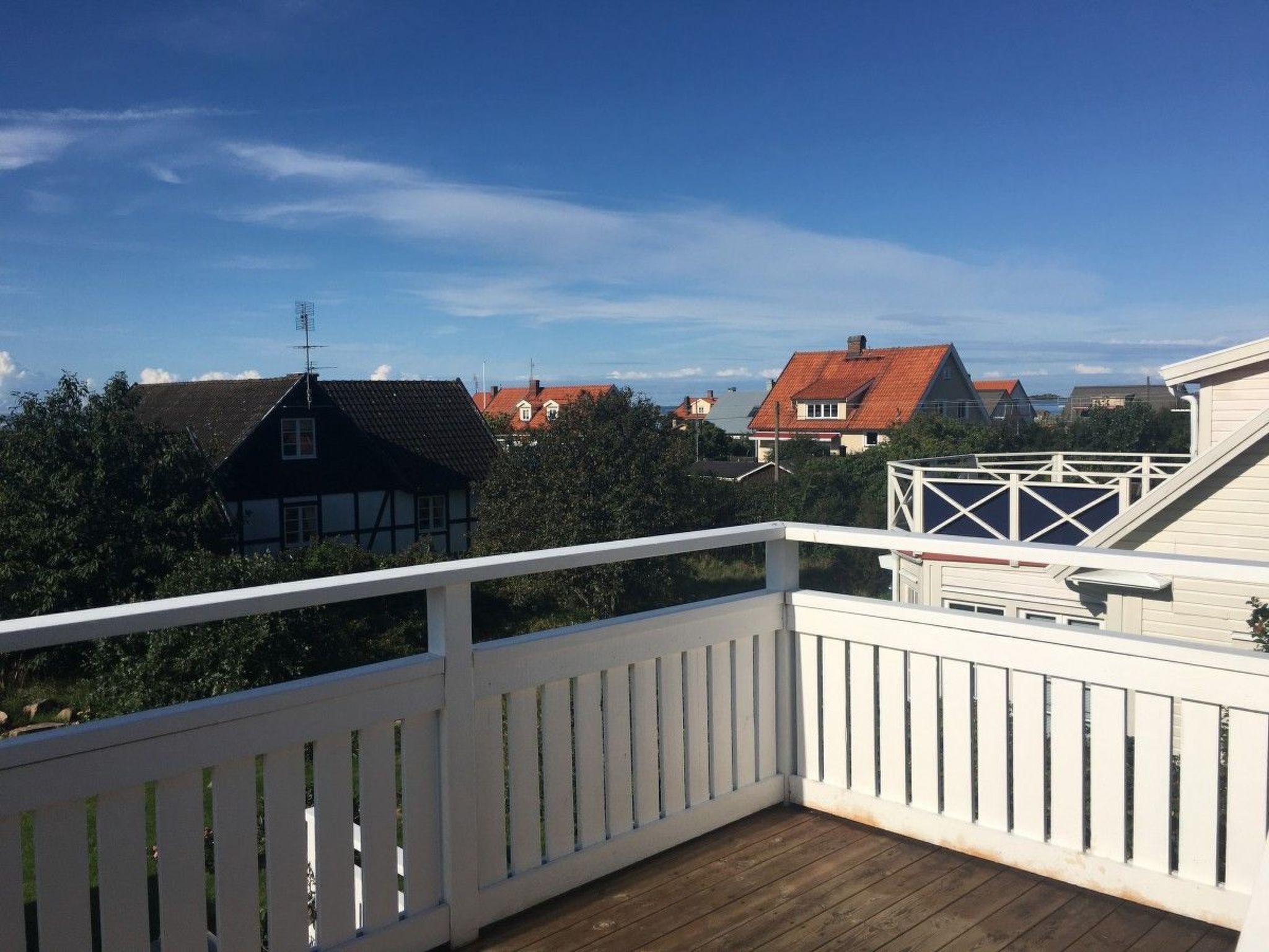 A wooden deck with white railings, overlooking a residential area with houses and trees.