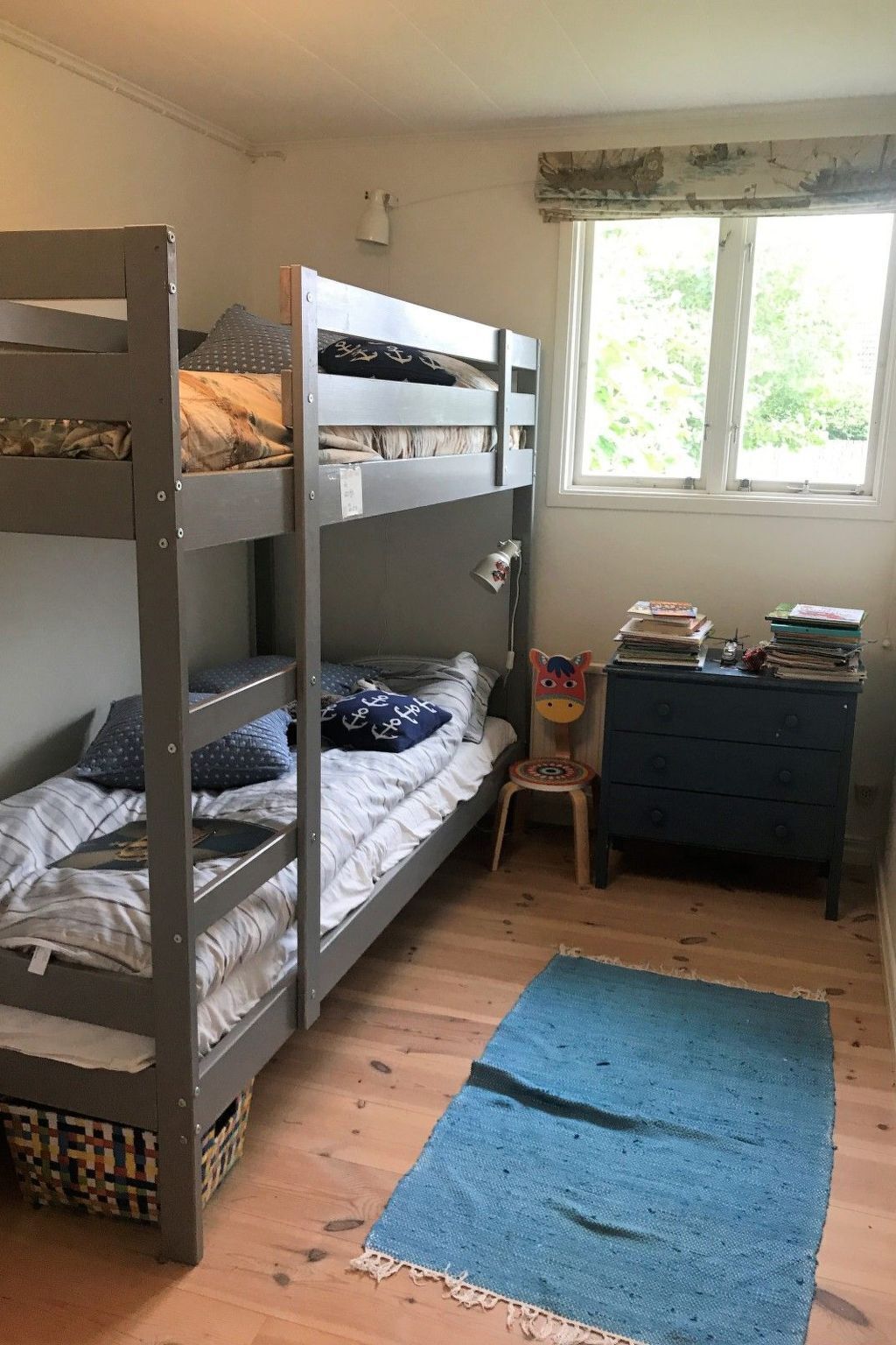 A bunk bed room with a desk and chair, a window with a view, and a blue rug.